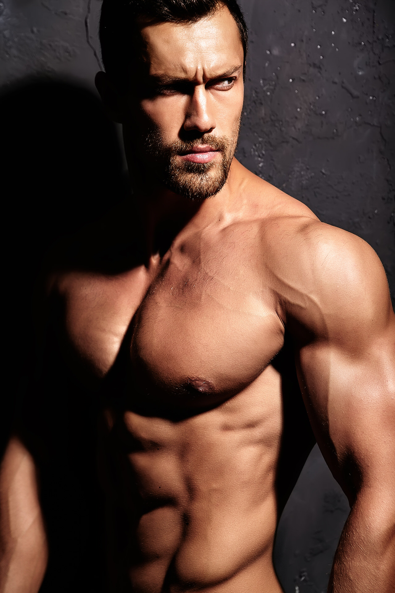 Portrait of strong healthy handsome Athletic Man Fitness Model posing near dark gray wall